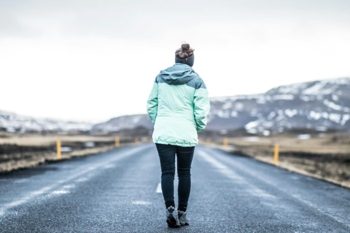Photo by Annie Niemaszyk woman wearing teal jacket and black pants walking on concrete road