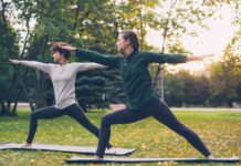 “벽을 넘어 숲으로”… 마음의 병 치유하는 ‘그린 엑서사이즈’ 열풍 Two women practicing yoga warrior pose outdoors.
