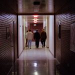 일상에 스며드는 근육 건강, 집에서도 작게 시작하세요 People walk down a dark, brick-walled hallway.