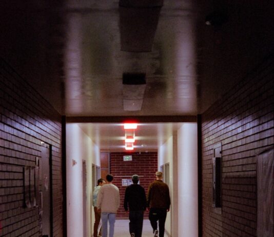일상에 스며드는 근육 건강, 집에서도 작게 시작하세요 People walk down a dark, brick-walled hallway.