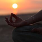 “마음챙김 명상, 바쁜 일상 속 스트레스 해소법으로 주목” A person sitting in a yoga position with the sun setting in the background